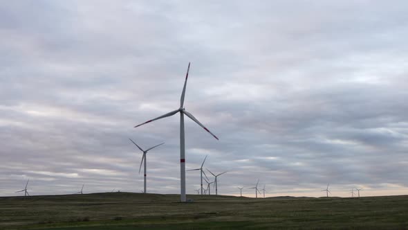 Motion the Blades of a Large Wind Turbine in a Field Against a Background of Orange Sunset on the