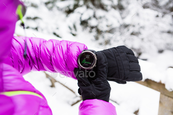 , smartwatch with altimeter app in winter woods and mountains. Female trekker trekking in white snowy forest with electronics wearable technology.