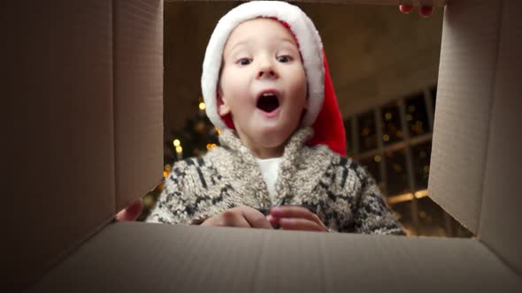 Happy Boy in a Santa Claus Hat Looks Into a Gift Box