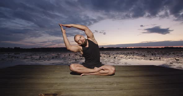 A Man Does Yoga on the River Bank During Sunset in Summer
