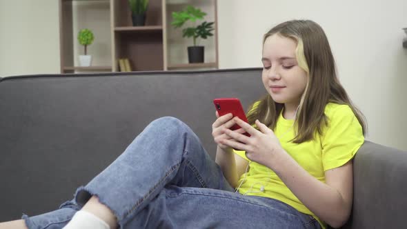 The Little Girl is Smiling and Looking at Her Phone While Sitting on the Couch