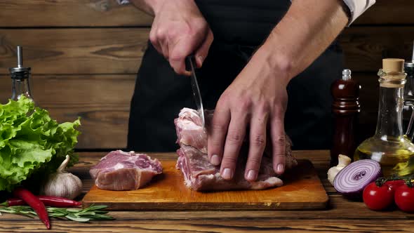 The Chef Cuts the Meat with a Knife on the Kitchen Table