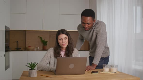 Young Mixed Race Couple are Discussing Something in Front of a Laptop in Their Kitchen at Home