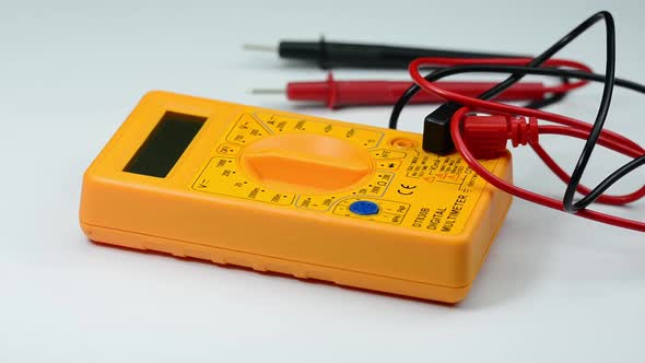 Yellow digital multimeter rotating on white plate