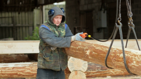 Builder Raises Wooden Timber With Overhead Winch Crane. A Man Holds a Log And Transfer It