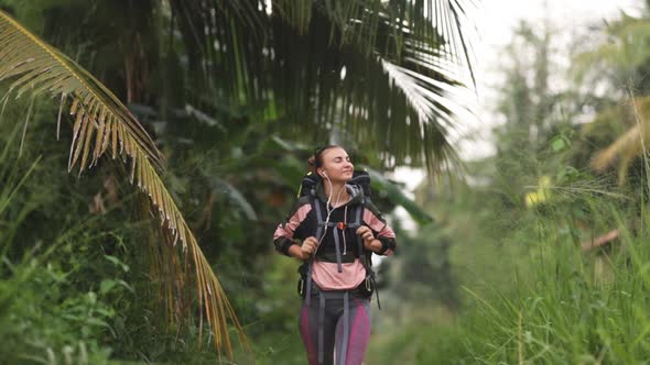 A white Caucasian girl with a large backpack is walking along a trail in tropical terrain.