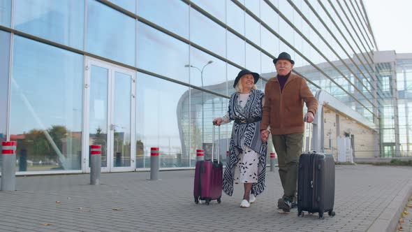 Senior Pensioner Tourists Grandmother Grandfather Walking From Airport Hall with Luggage on Wheels