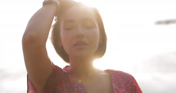 Lovable Brunette Woman Touching Hair at the Sea Sunset