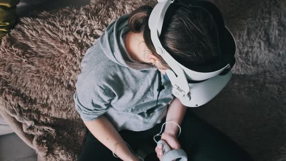 Young Woman in Virtual Reality Helmet Sitting on Sofa and Move Hands at Home