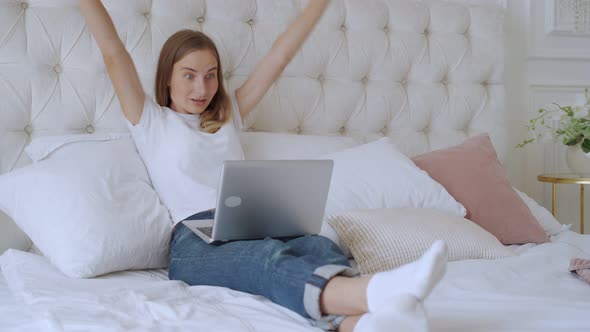 Young Woman Sitting on the Bed with Laptop Cheering Carefree and Excited, Victory Concept