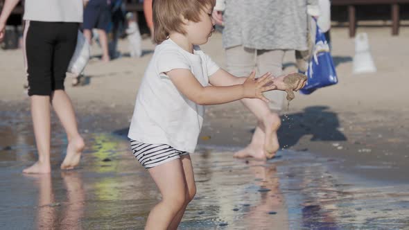 Toddler Boy in Swimwear Is Playing with Sand on Sea Side.