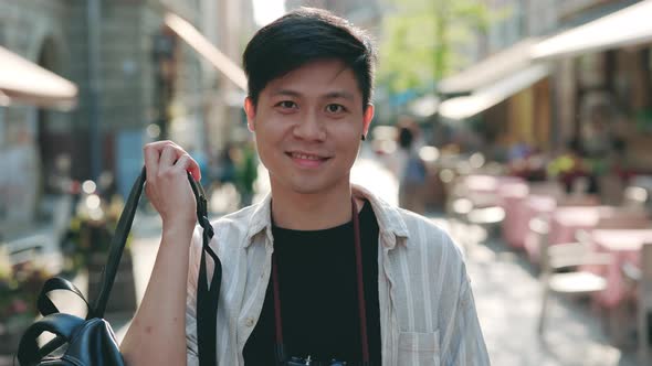 Positive Asian Guy with Retro Camera Posing on City Street
