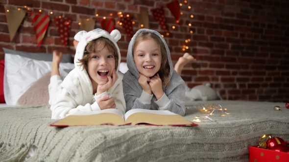 Cute Smiling Sister And Brother Reading a Book And Laughing At The Home In a Christmas Time. They