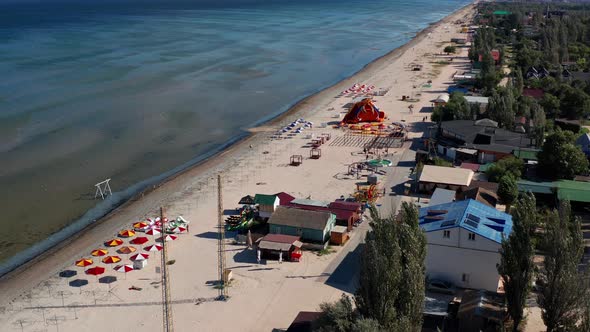 Beautiful flight in summer over the beach. Beach umbrellas, rides, people swimming in the sea.