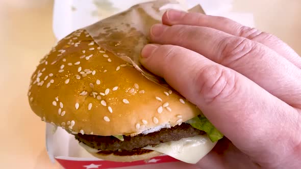 A large burger with beef, cheese, sauce, tomatoes and a lettuce in someone's hand