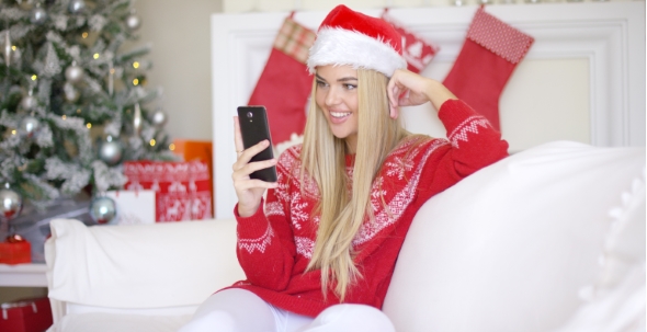 Young Happy Blond Girl In Christmas Outfit Using Mobile Phone