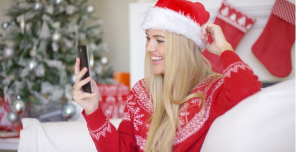 Young Happy Blond Girl In Christmas Outfit Using Mobile Phone