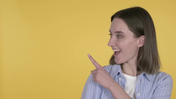 Pointing Young Woman Showing Product, Yellow Background