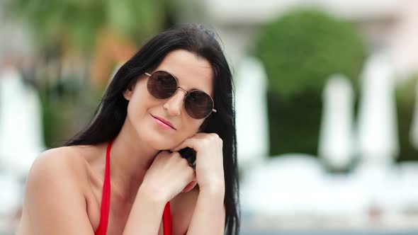 Portrait of Relaxed Female in Sunglasses with Waving Hair Smiling Posing on Beach Closeup