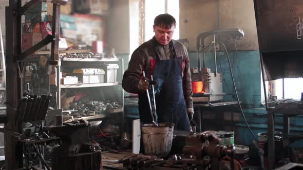 Man Blacksmith Takes Out Heated Metal Detail Out of the Furnace and Cooling Down in a Bucket of