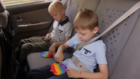 Two Little Brothers are Sitting in the Car and Playing an Antistress Toy Pop It