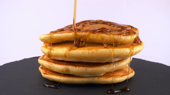 American pancakes with maple syrup on a white background. Pancake lies on a black slate round stone.
