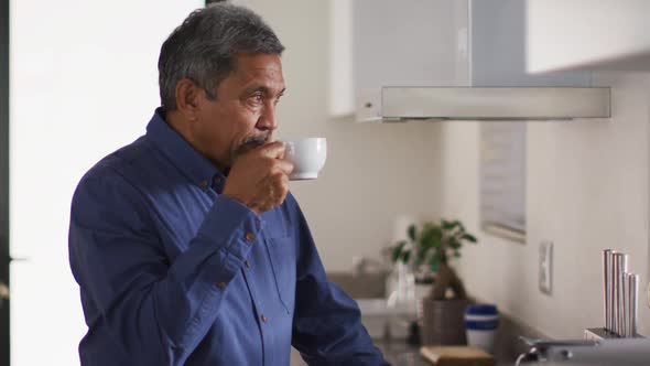 Senior mixed race man in kitchen drinking coffee