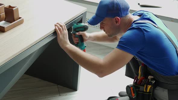 Male Handyman Using an Electric Screwdriver Tool in His Hand and Repairing a Wooden Table