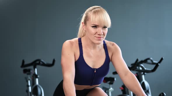 Smiling Fitness Woman in Sportswear Riding on Exercise Bike at Gym