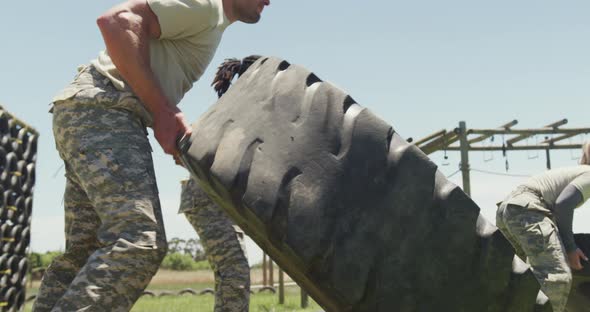 Fit diverse group of soldiers flipping tractor tyres on army obstacle course in the sun