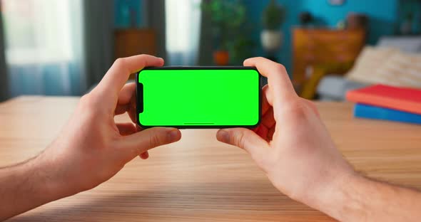 Closeup of Man Using Green Mockup Screen Smartphone in Landscape Mode While Sitting at His