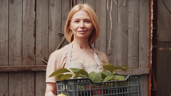 Happy Female Farmer Holding Crate with Plants and Smiling at Camera
