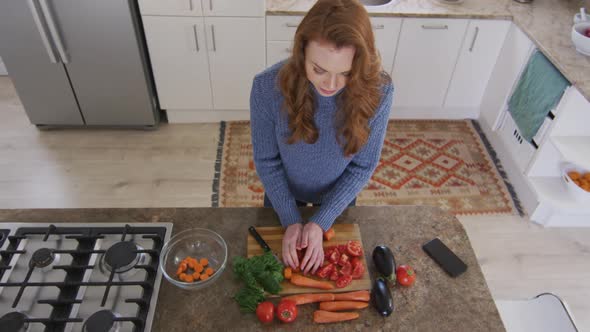 Top view of woman chopping vegetables and putting it in bowl in the kitchen