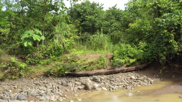 Zooming out on a large wooden canoe that lays on a riverbed of a large tropical river