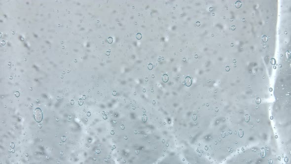 Transparent Blue Cosmetic Gel Fluid with Bubbles Flowing Down on a White Surface