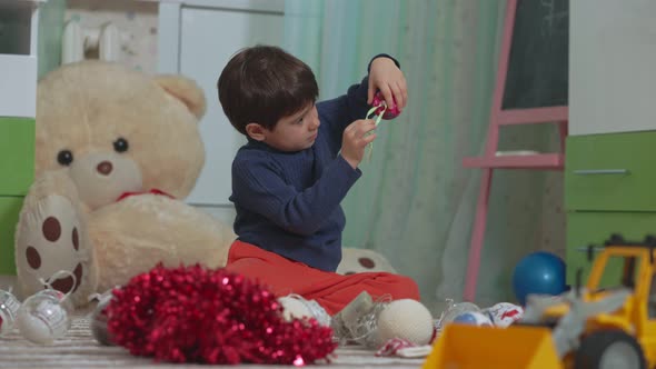 Little Baby Boy Chooses Christmas Tree Toys on the Floor of His Children's Room Against the