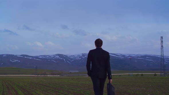 Businessman in suit and business bag walking in field.