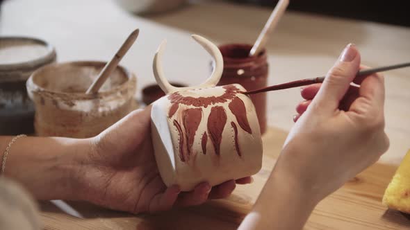 Young Woman Potter Painting on the Ceramic Cup with a Brush