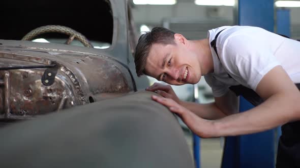 Cheerful Young Service Man Examining Old Classic Retro Car with Admiration Before Restoration Work