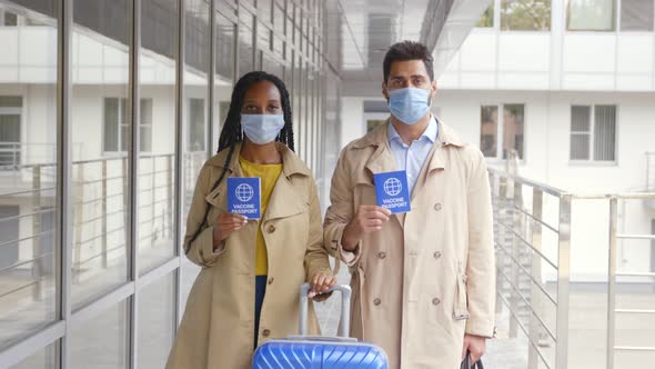 Dolly Push Shot of Diverse Couple Travelers in Safety Mask with Suitcase and Vaccination Passport