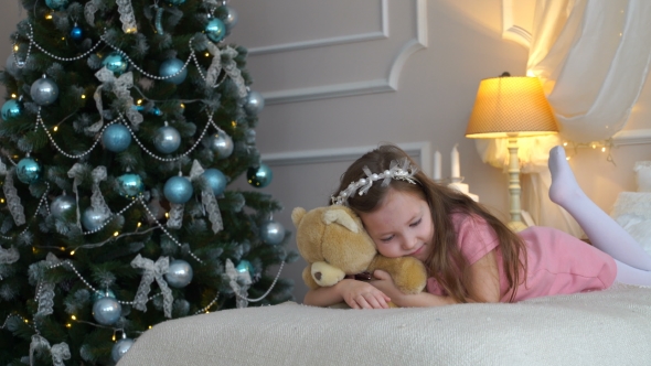 Woman Lies On a Bed With a Teddy Bear Near a Christmas Tree
