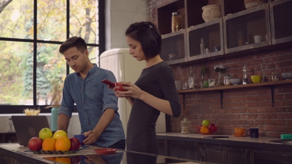 Two People Holding Cups And Use Gadgets Indoors.
