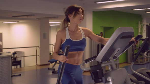 Slim Girl With Shapely Brawny Body Using Elliptical Trainers For Warm Up.