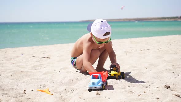 Happy Baby Playing with Cars on the Beach, on the Horizon Azure Sea and Blue Sky