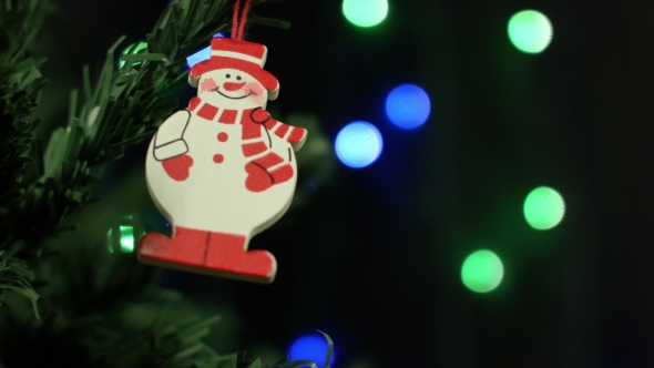 Snowman And Christmas Ornaments For The Christmas Tree On The Background Of Lights