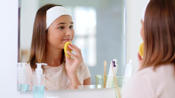 Teenage Girl Cleaning Face with Sponge at Bathroom