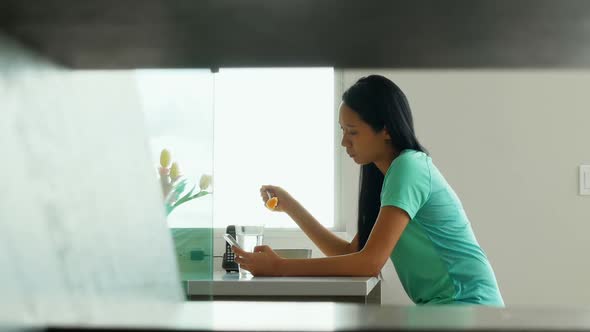 Woman using mobile phone while having breakfast in kitchen