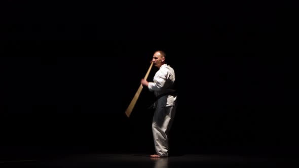 Kendo Fighter on White Kimono Practicing Martial Art with the Bamboo Bokken on Black Background.