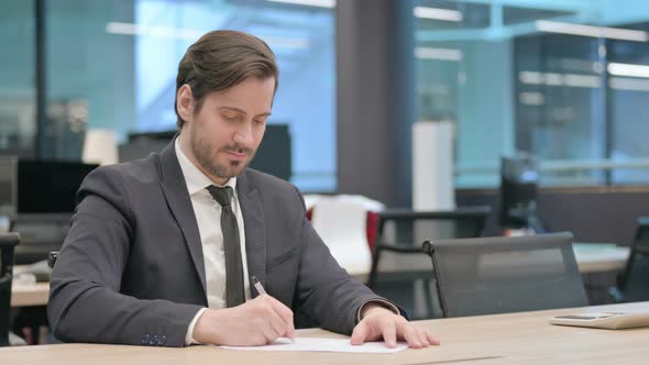 Businessman Writing on Paper in Office Paperwork