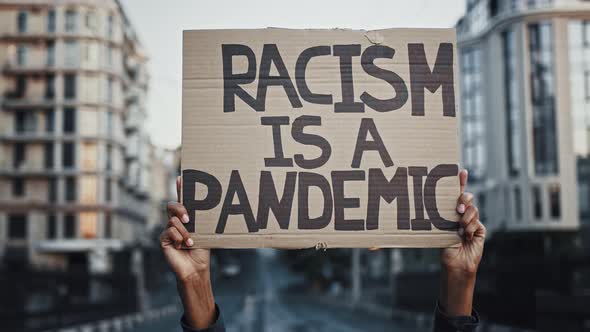 Hands of Unknown Africanamerican Person are Raising Up Cardboard Poster Racism is a Pandemic Posing